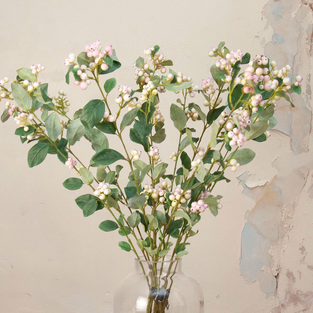 Close up Artificial Snowberry Stems with soft pink and white berry clusters and realistic green foliage displayed in a clear glass vase
