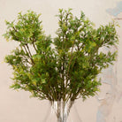 Close up Artificial Autumnal Fern Foliage Stems with delicate green and yellow-toned foliage displayed in a clear ribbed glass vase
