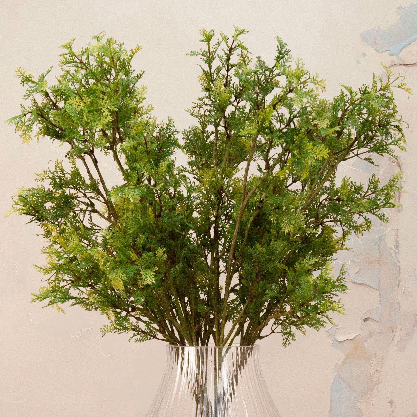 Close up Artificial Autumnal Fern Foliage Stems with delicate green and yellow-toned foliage displayed in a clear ribbed glass vase