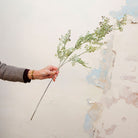 Hand holding muted green artificial shell fern greenery stem