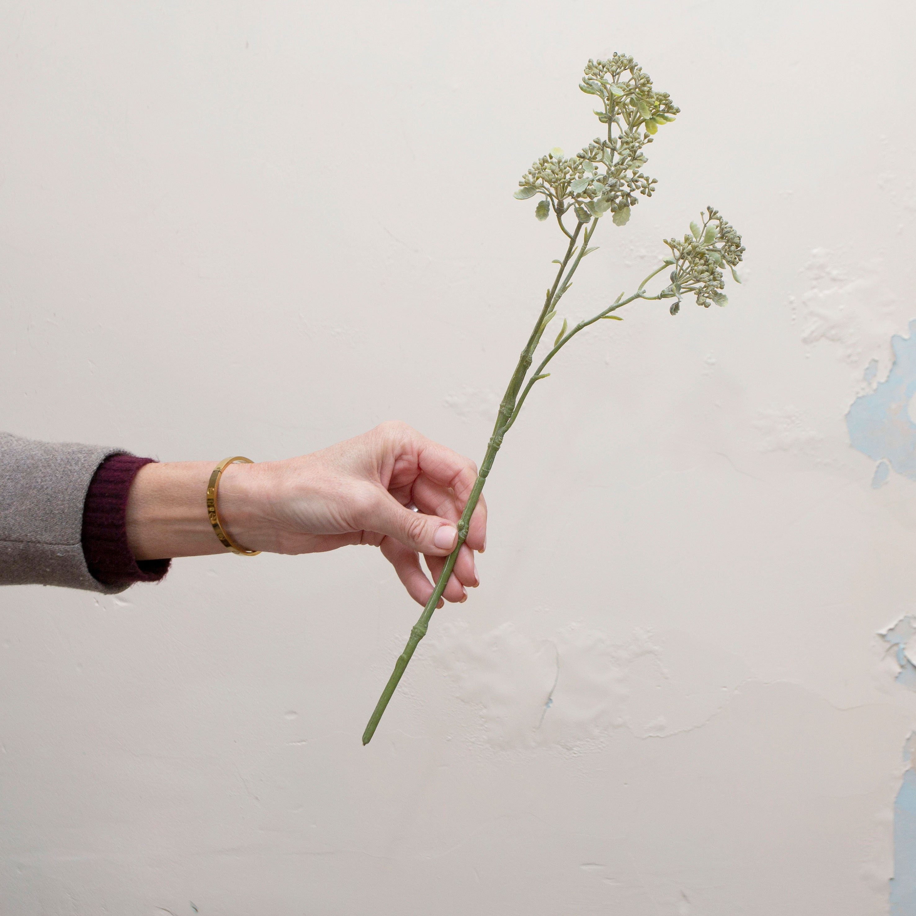 Artificial soft green patrinia spray stem held in hand, featuring delicate clustered flowers on fine branching stems