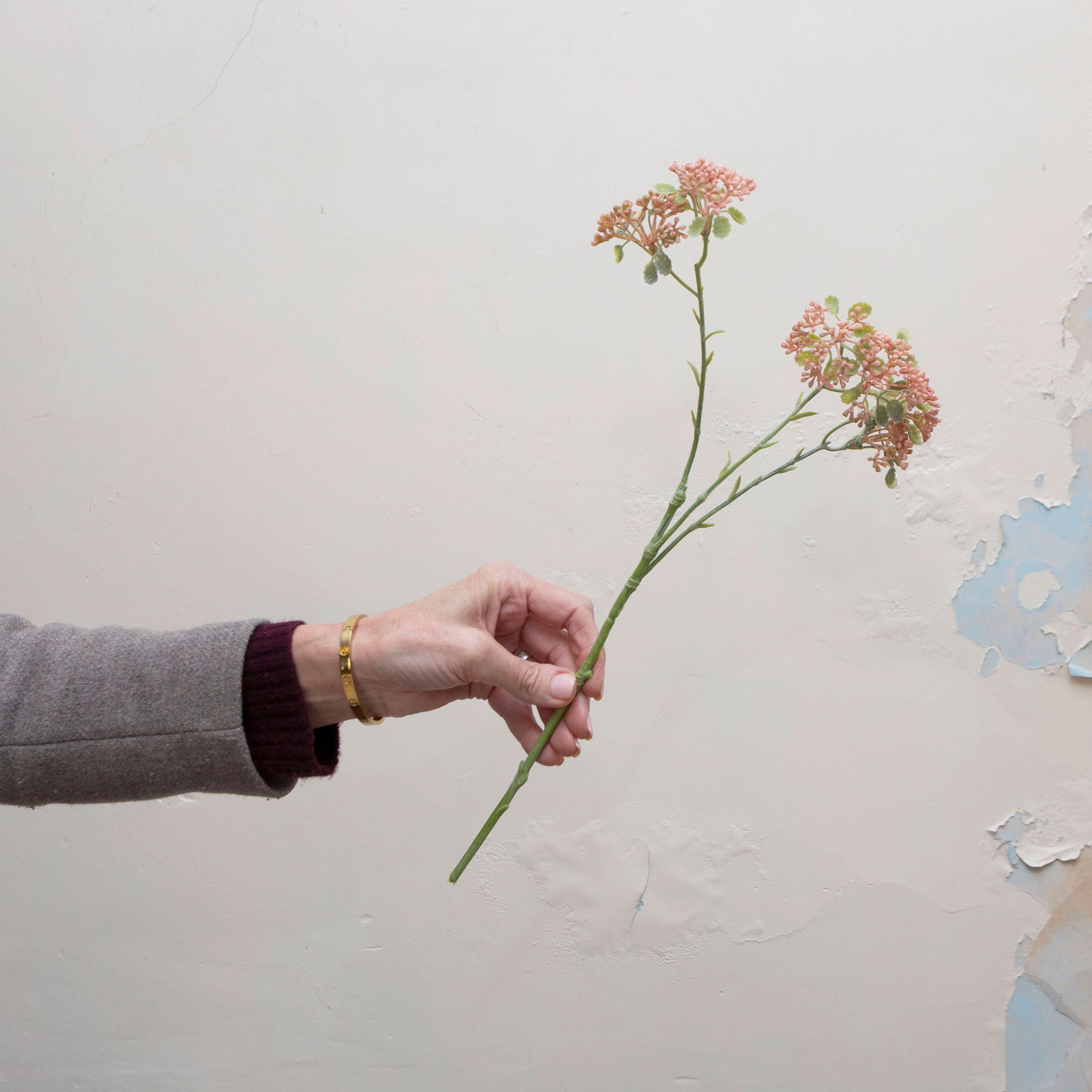 Artificial soft pink-peach patrinia spray stem held in hand, featuring delicate clustered flowers on fine branching stems.