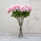 Artificial pink peony stems with green leaves displayed in vase  