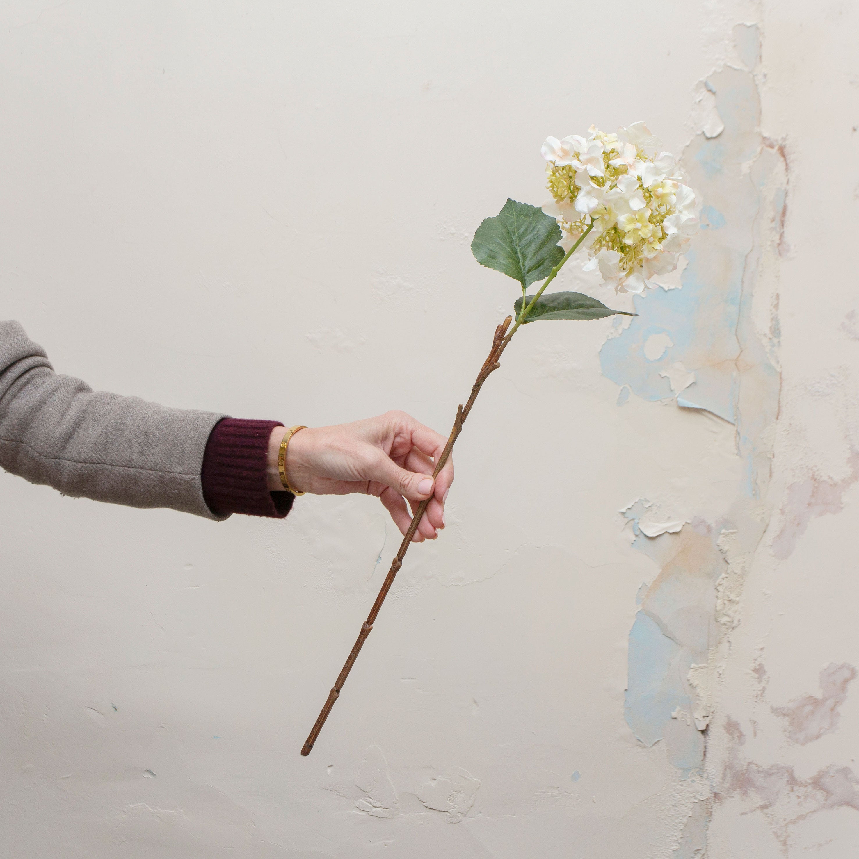 Artificial soft cream seeded hydrangea stem with peach detailing held in hand, featuring clustered blooms and green leaves.