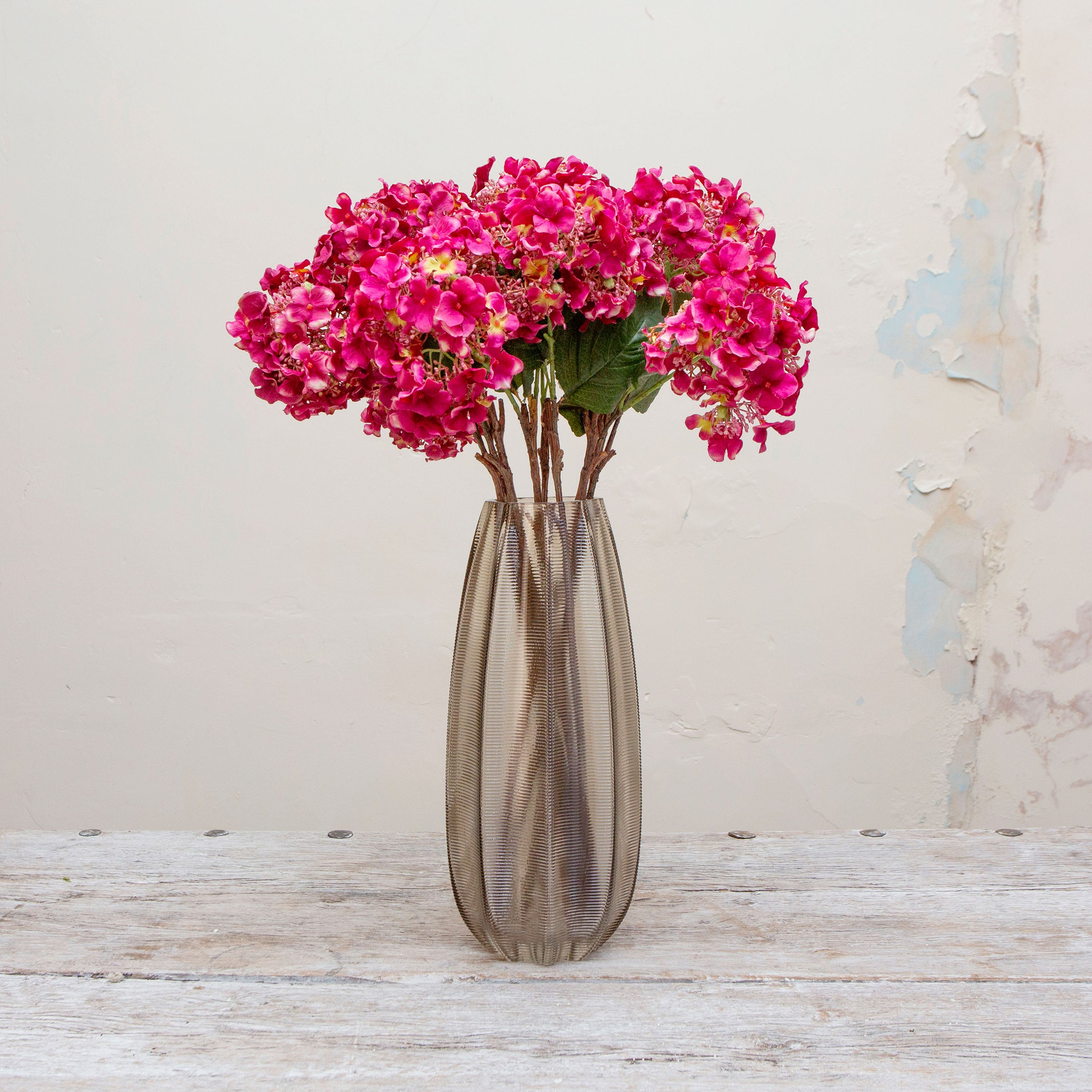 Artificial bright pink hydrangea stems displayed together in a vase for styling purposes.