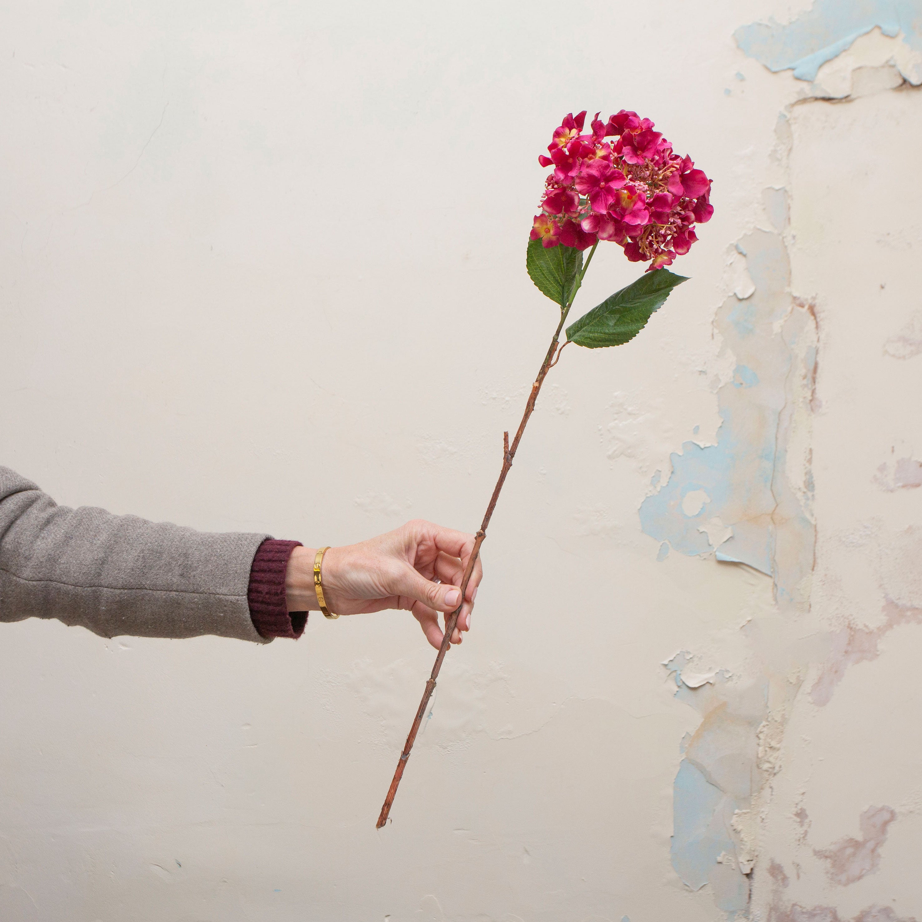 Artificial bright pink hydrangea stem held in hand, featuring clustered blooms and green leaves on a woody stem.
