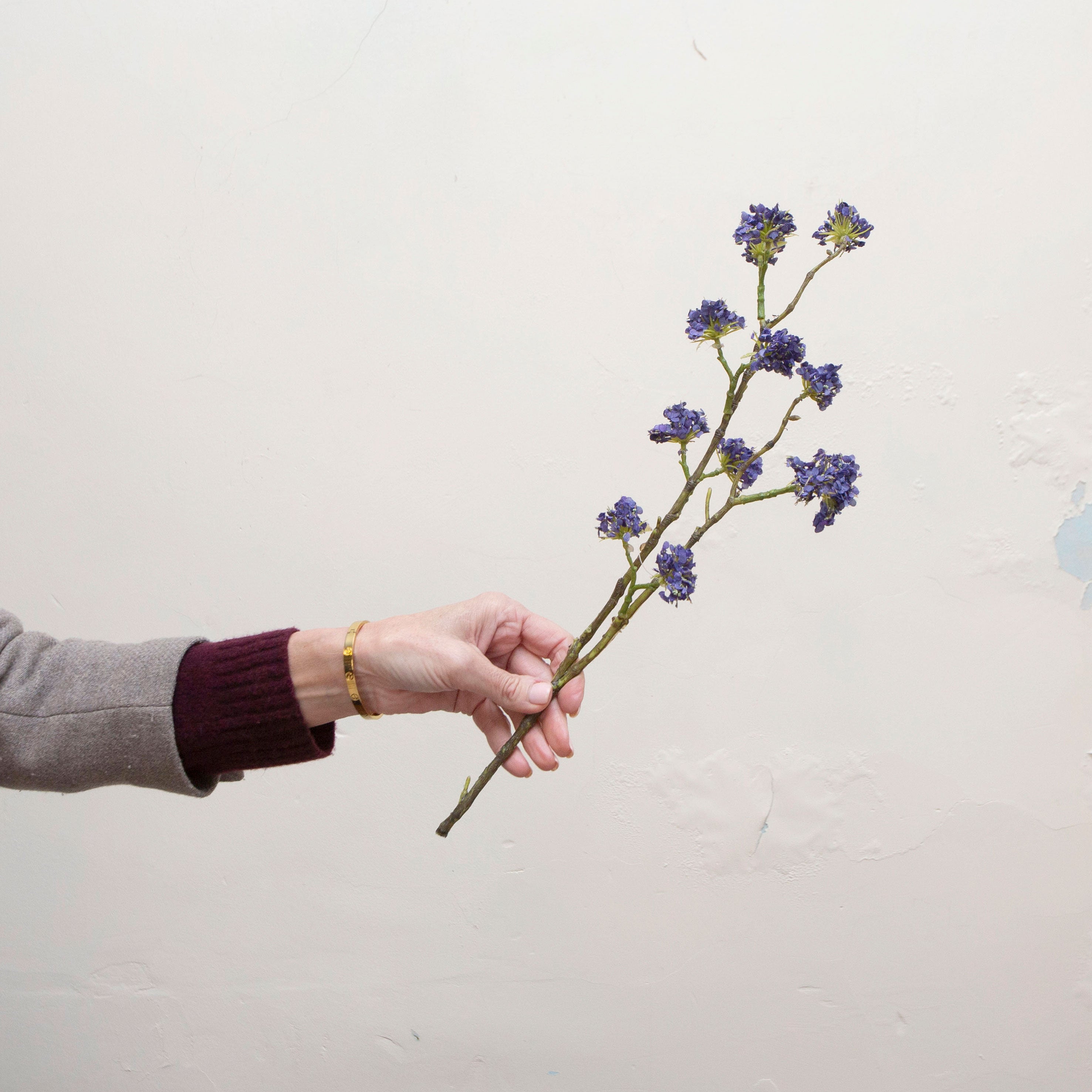 Artificial purple blue buddleia spray stem held in hand, featuring clustered blue flowers on branching stems.