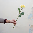 rtificial yellow rose stem held in hand, featuring layered petals and realistic green leaves.