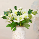 Close up Artificial Hellebore Stems with delicate white flowers, soft green centres, buds and realistic green foliage displayed in a textured white ceramic vase
