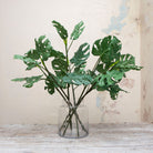 Artificial green tropical monstera leaf stems displayed in vase 
