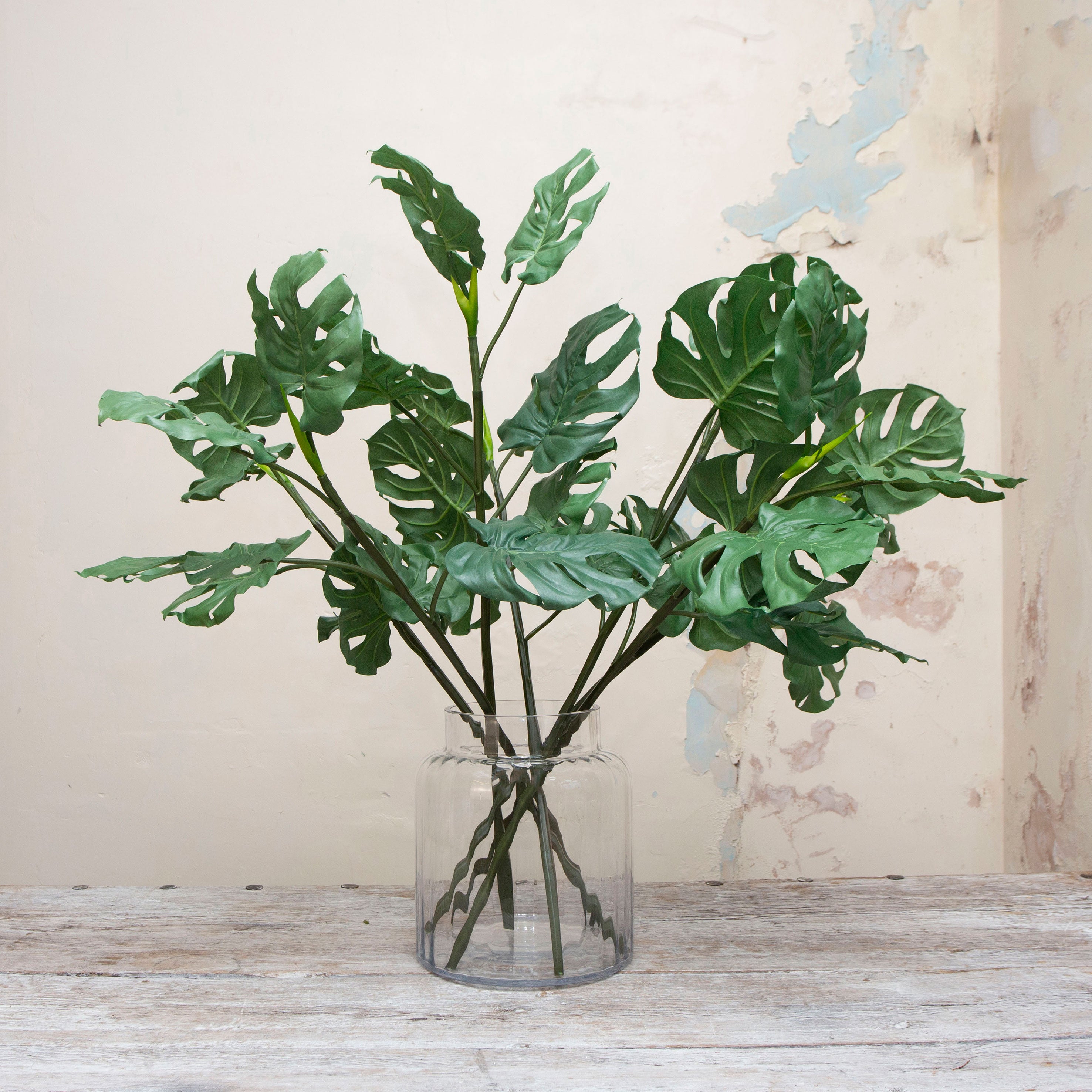 Artificial green tropical monstera leaf stems displayed in vase 