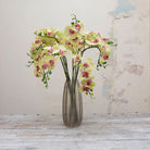 Artificial green orchid stems with pink detailing displayed together in a vase for styling purposes.