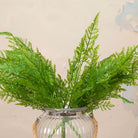Close up of Artificial Fern Bush Stems with lush, feathery green fern foliage displayed in a clear ribbed glass vase with rope handle