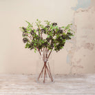 Artificial Berry Stems with clusters of dark purple-black berries, fresh green leaves and natural brown branches displayed in a clear glass vase
