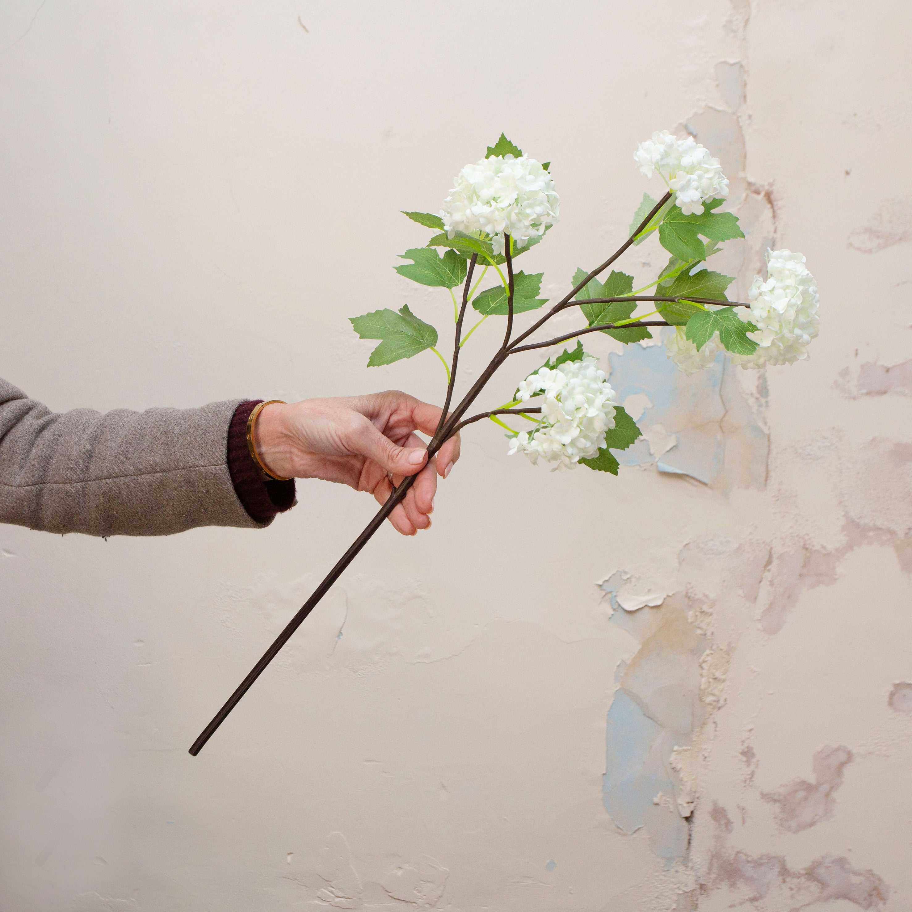 Hand holding artificial white snowball stems with green leaves displayed