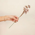 Hand holding Artificial Berry Pick Stem with clusters of soft pink and mauve berries 