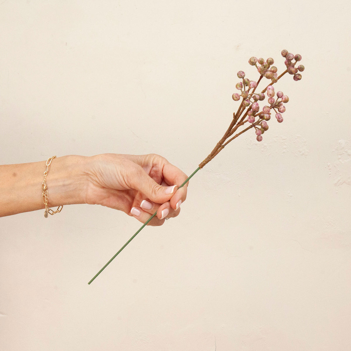 Hand holding Artificial Berry Pick Stem with clusters of soft pink and mauve berries 