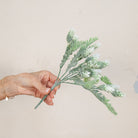 Hand holding Artificial Pine Cone Fern Flocked Stem with frosted green fern foliage, soft white flocked tips and pine cone detailing