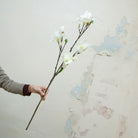 Hand holding white artificial magnolia on a long brown stem
