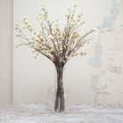 Artificial cream blossom stems with yellow centres on long brown branches displayed in vase 