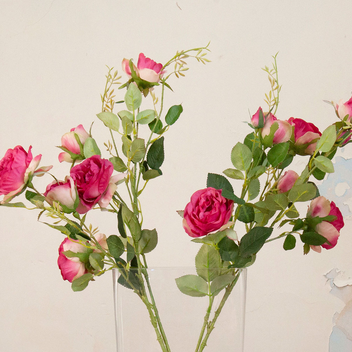 Close up of Artificial Julie Rose Spray Stems with vibrant pink rose blooms, soft pink buds and realistic green foliage displayed in a tall clear glass vase