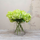 Large headed artificial bright lime green hydrangea stems with leaves displayed in vase 