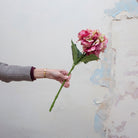 Hand holding artificial hydrangea stem with mixed pink and cream petals