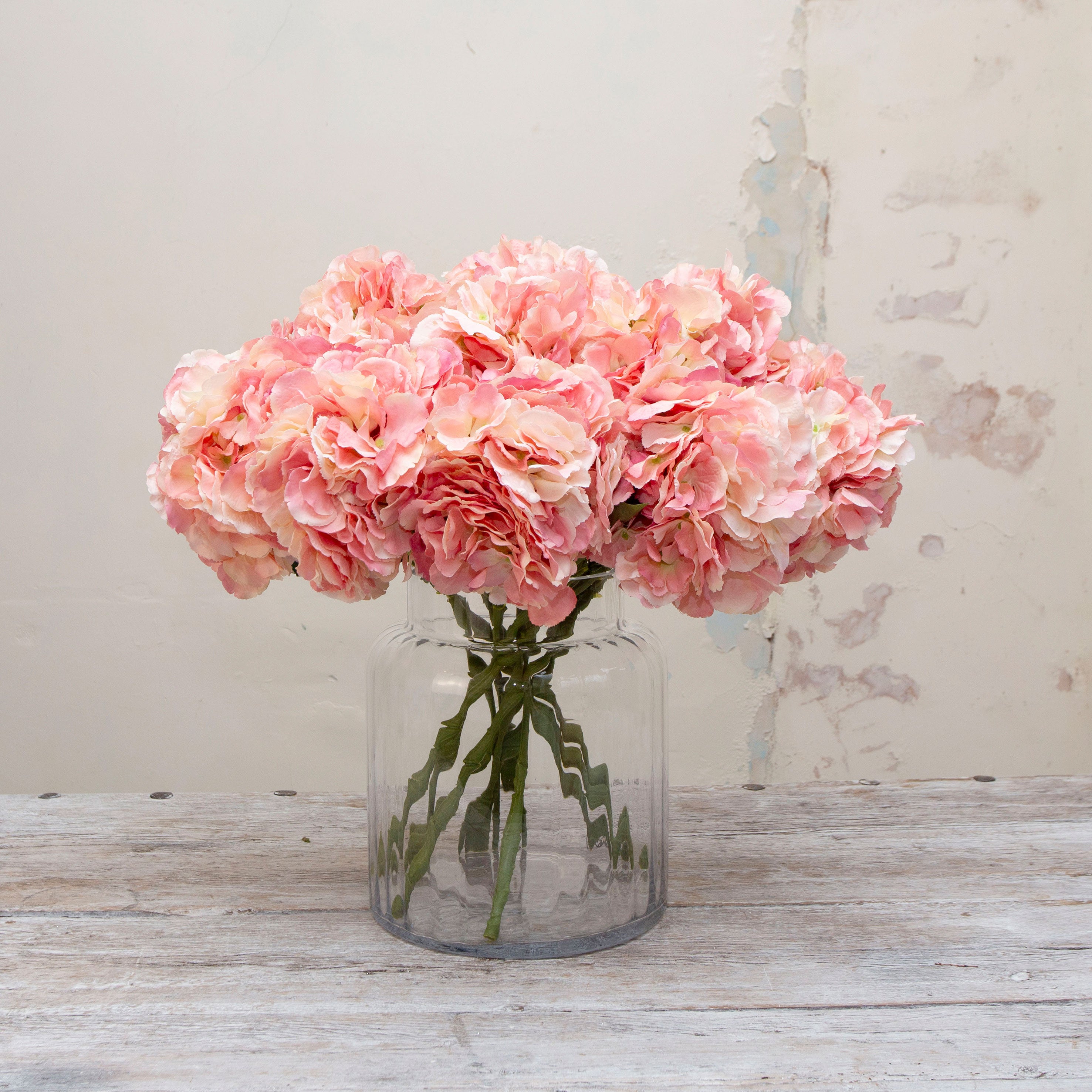 Artificial peach-pink hydrangea stem displayed in a vase, with a generous clustered bloom and realistic green foliage
