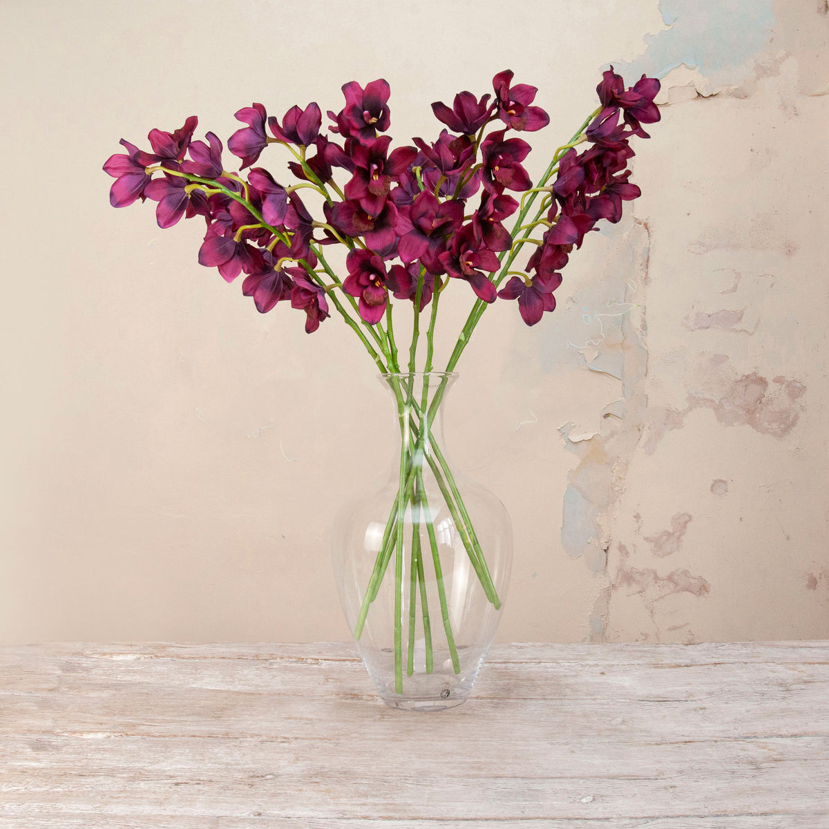 Artificial Plum Cymbidium Orchid Stems with rich deep plum blooms, delicate yellow centres and realistic green stems displayed in a clear glass vase
