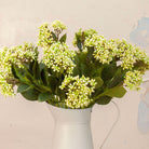 Close up of Artificial Berry Stems with clusters of cream and pale green berries, dark green leaves and natural brown branches displayed in a white metal jug