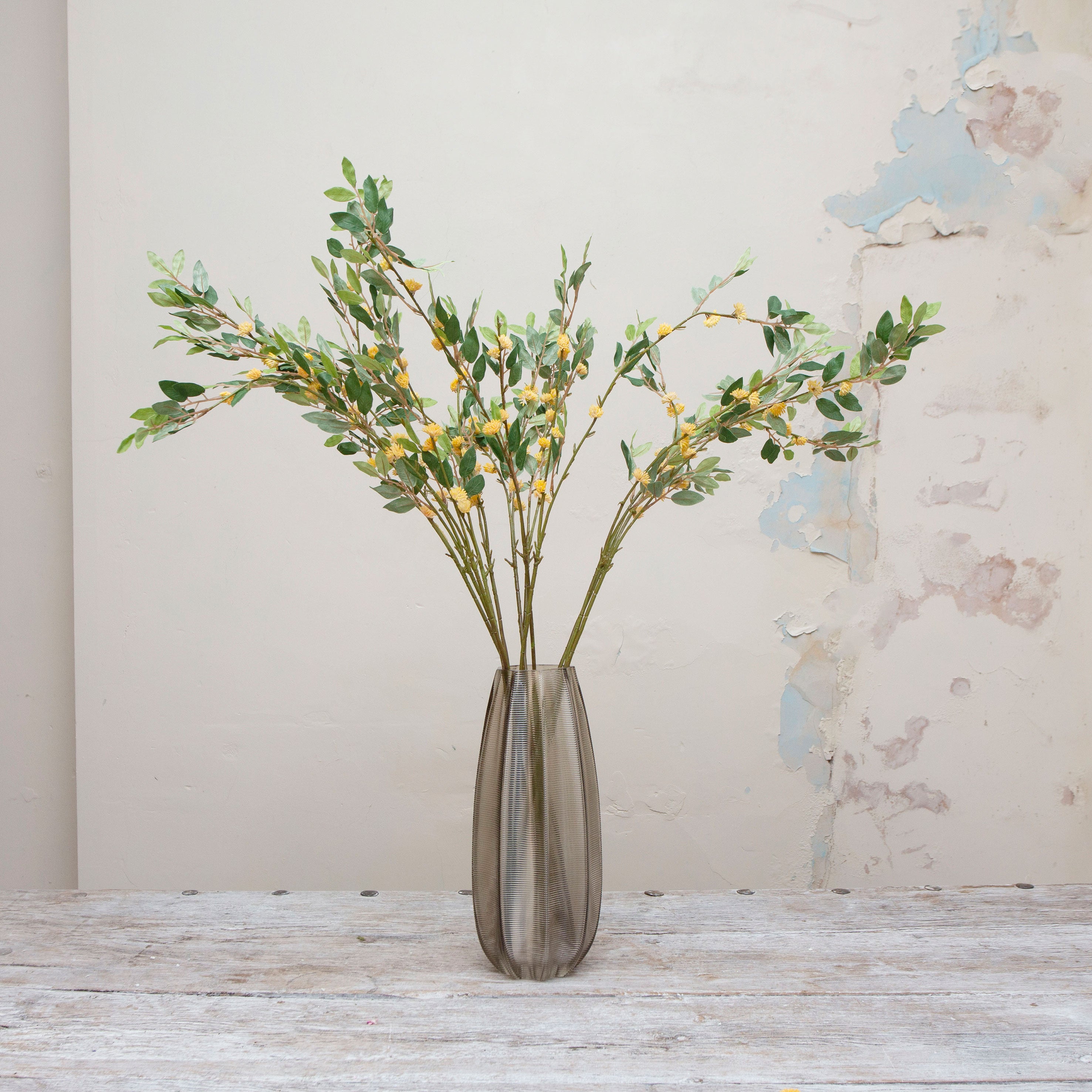 Artificial greenery stem with yellow seeds displayed in smoked glass vase 