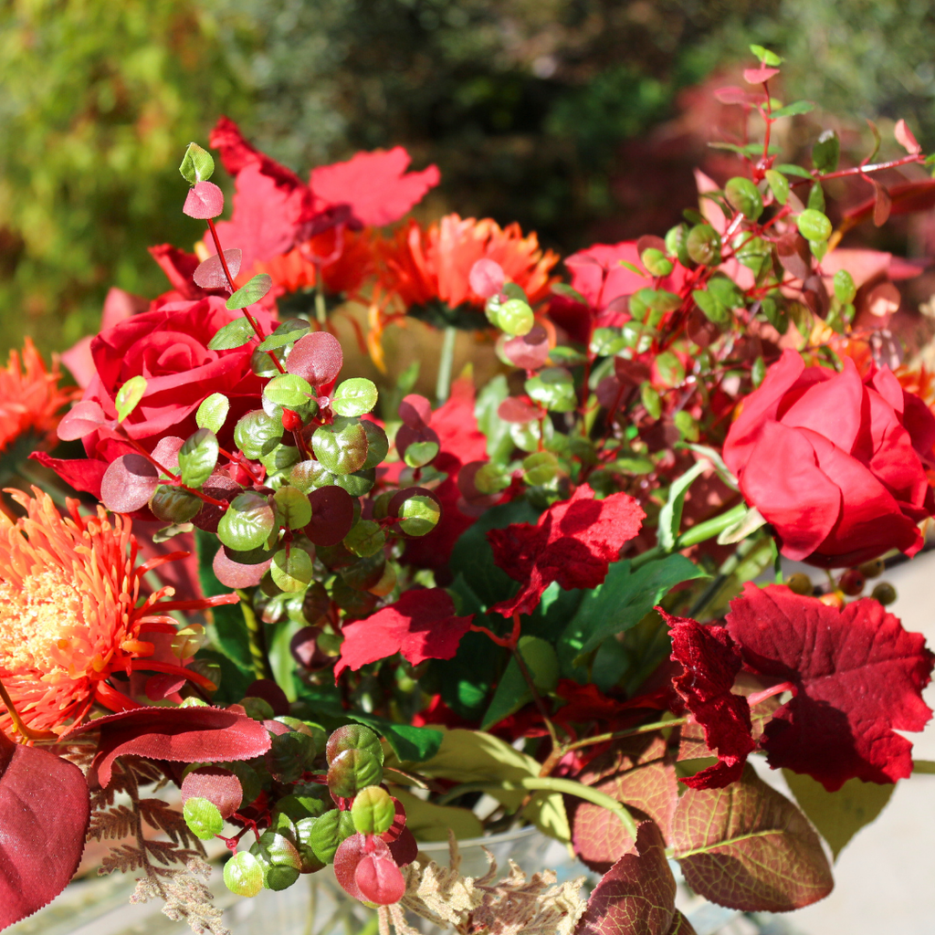 Vibrant Red Roses and Orange Autumn Chrysanthemums with Foliage in a Footed Vase Outside Close Up