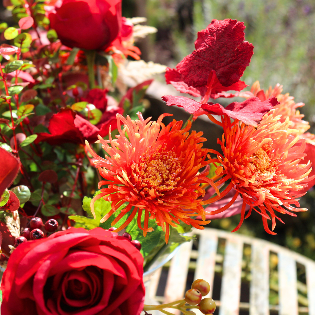 Vibrant Red Roses and Orange Autumn Chrysanthemums with Foliage in a Footed Vase Outside Close Up