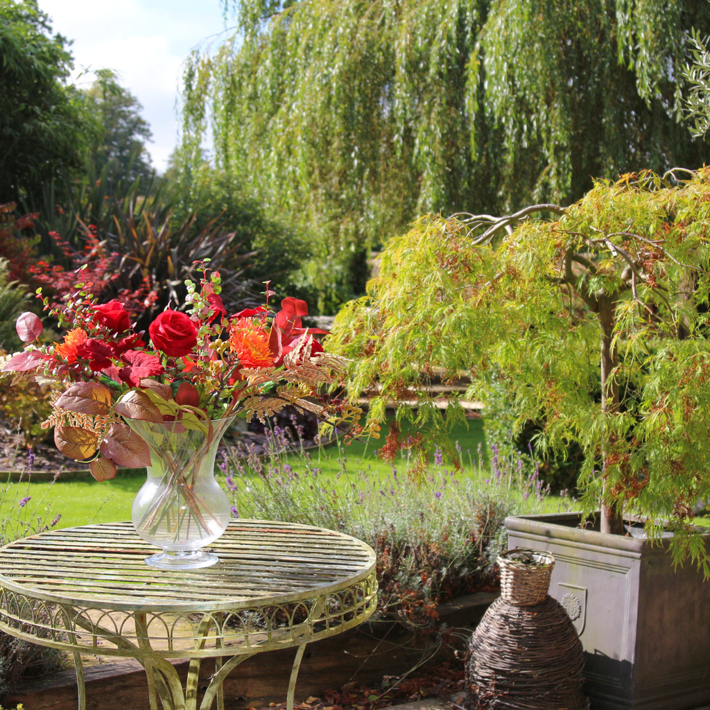 Vibrant Red Roses and Orange Autumn Chrysanthemums with Foliage in a Footed Vase Outside