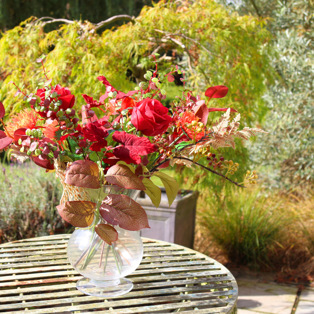 Vibrant Red Roses and Orange Autumn Chrysanthemums with Foliage in a Footed Vase Outside Close up