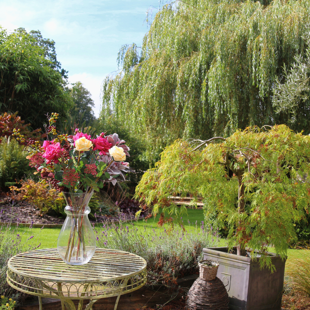 Large Glass Vase filled with breeds of Roses and Foliage Outside