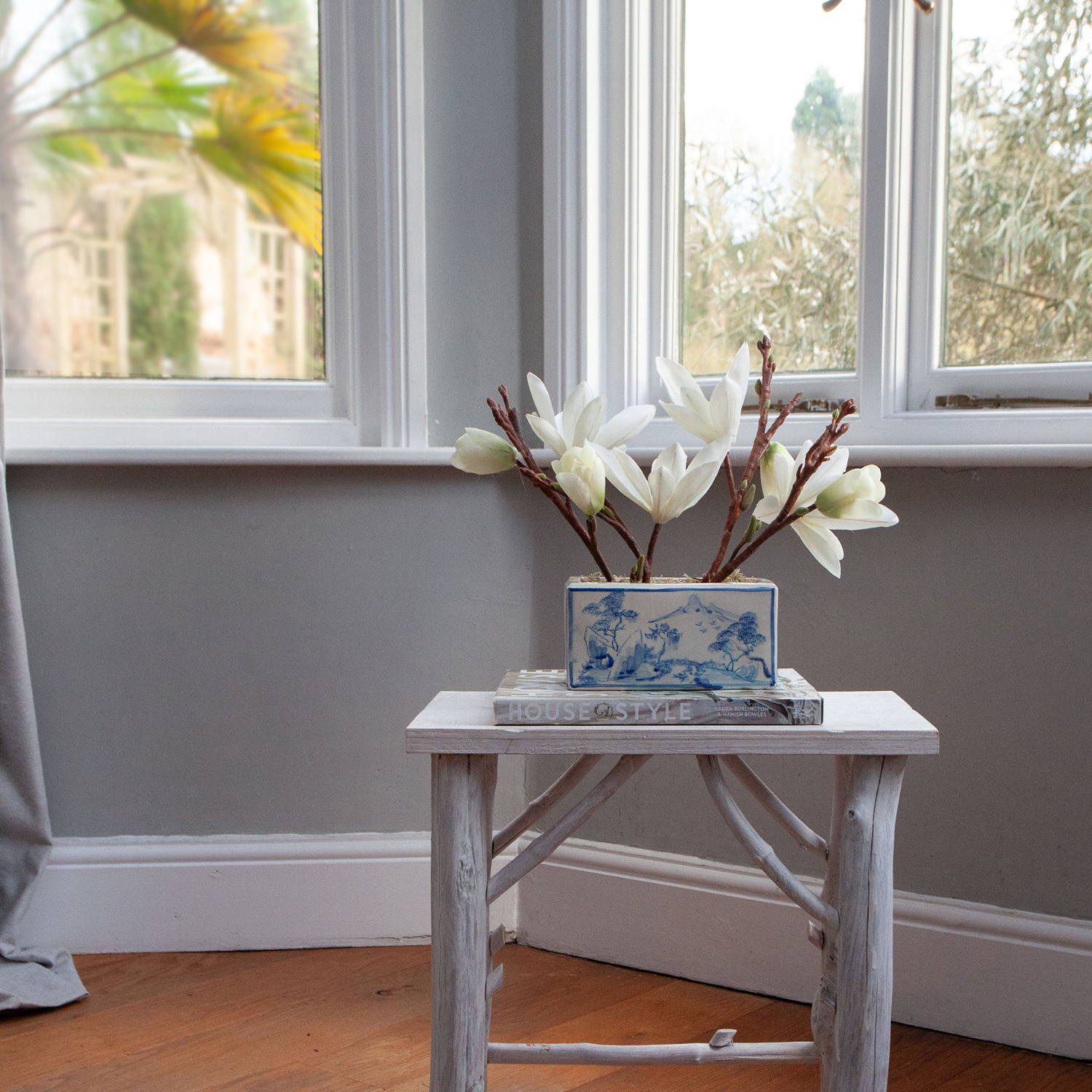 Artificial magnolia arrangement with white blooms displayed in a blue and white ceramic planter.