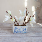 Artificial magnolia arrangement with white blooms displayed in a blue and white ceramic planter.