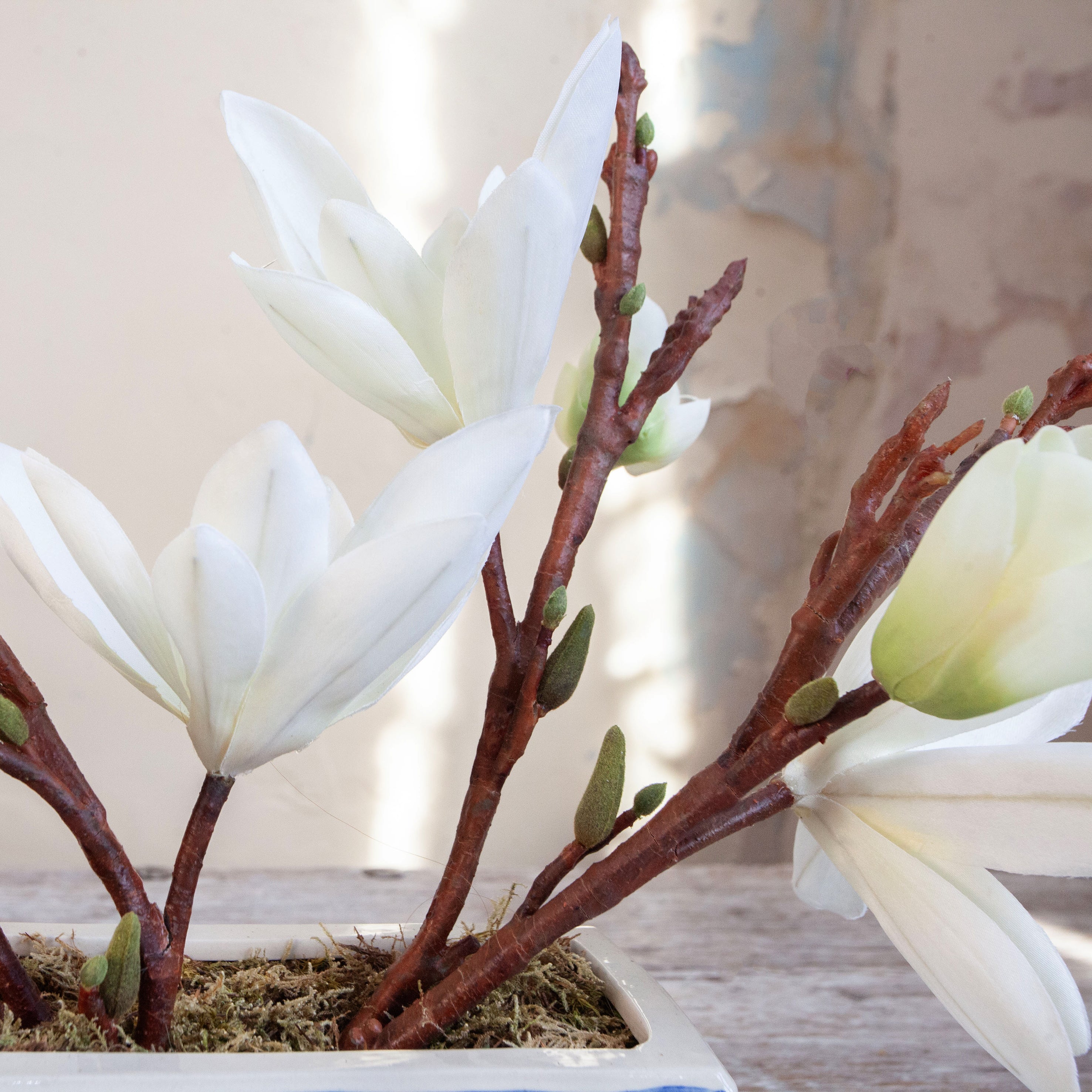 Artificial magnolia arrangement with white blooms displayed in a blue and white ceramic planter.