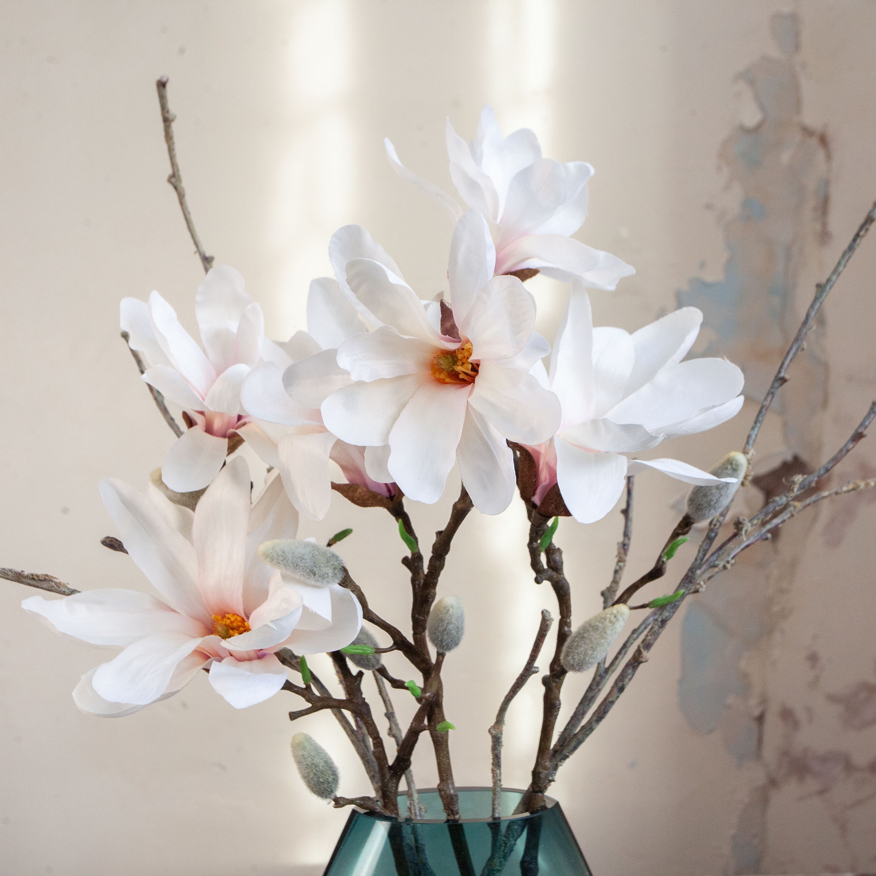 Artificial magnolia and branch arrangement with soft white blooms displayed in an ocean blue glass vase.