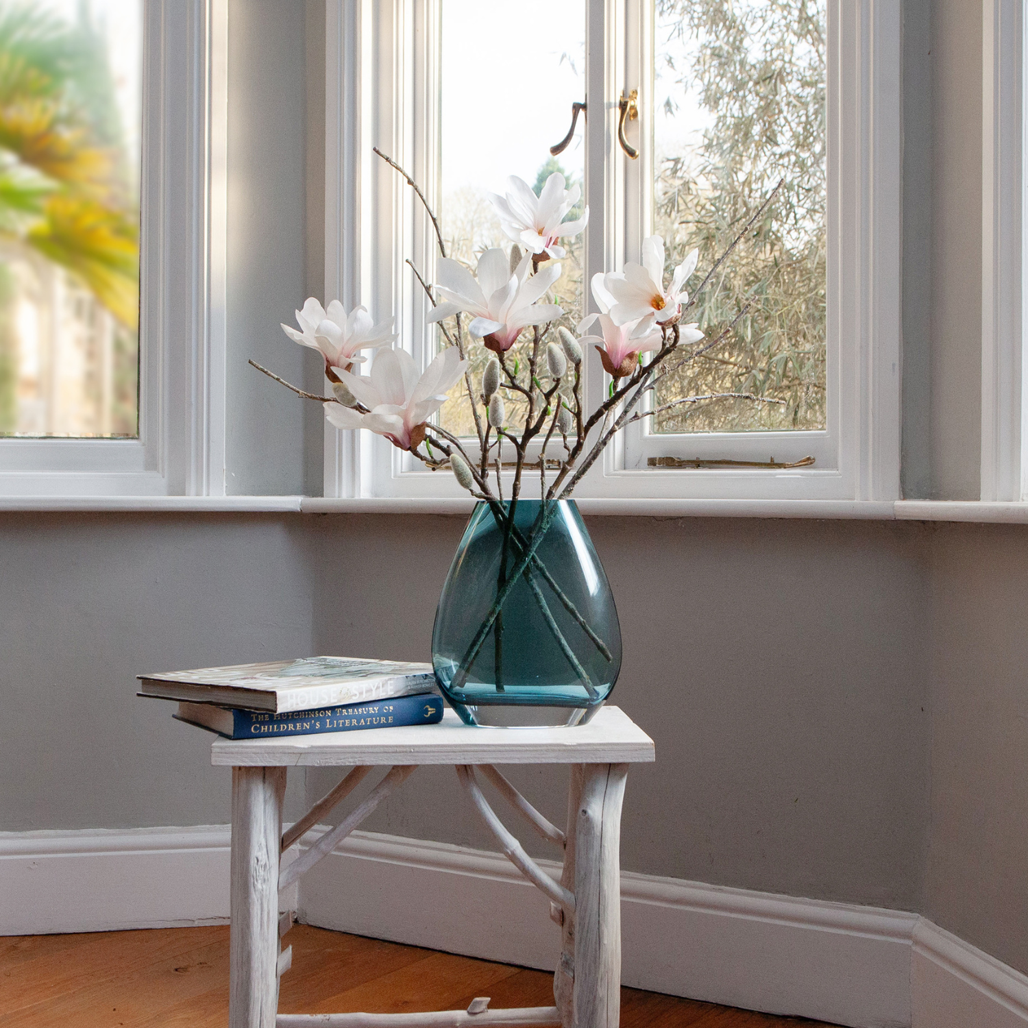 Artificial magnolia and branch arrangement with soft white blooms displayed in an ocean blue glass vase.