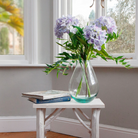 Artificial hydrangea and greenery arrangement in a teardrop-shaped vase,