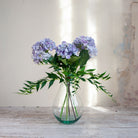 Artificial hydrangea and greenery arrangement in a teardrop-shaped vase,