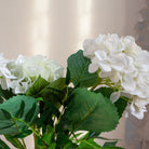 Artificial hydrangea and greenery arrangement in a teardrop-shaped vase,