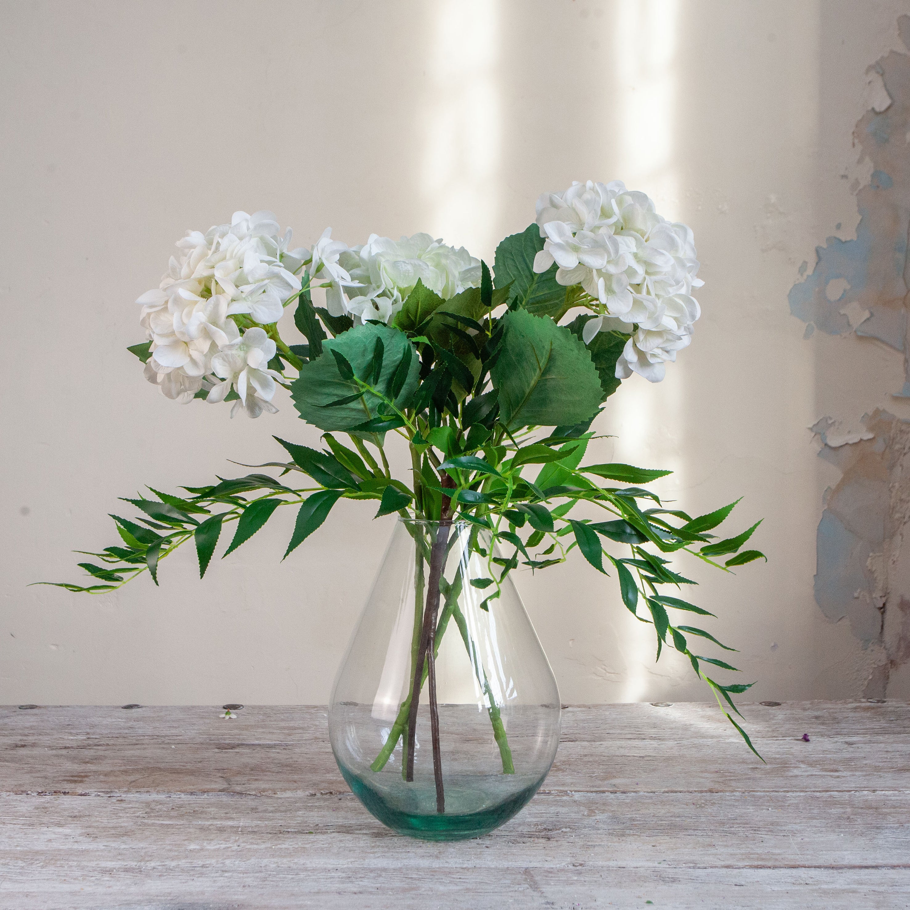 Artificial hydrangea and greenery arrangement in a teardrop-shaped vase,
