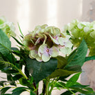 Artificial hydrangea and greenery arrangement in a teardrop-shaped vase,