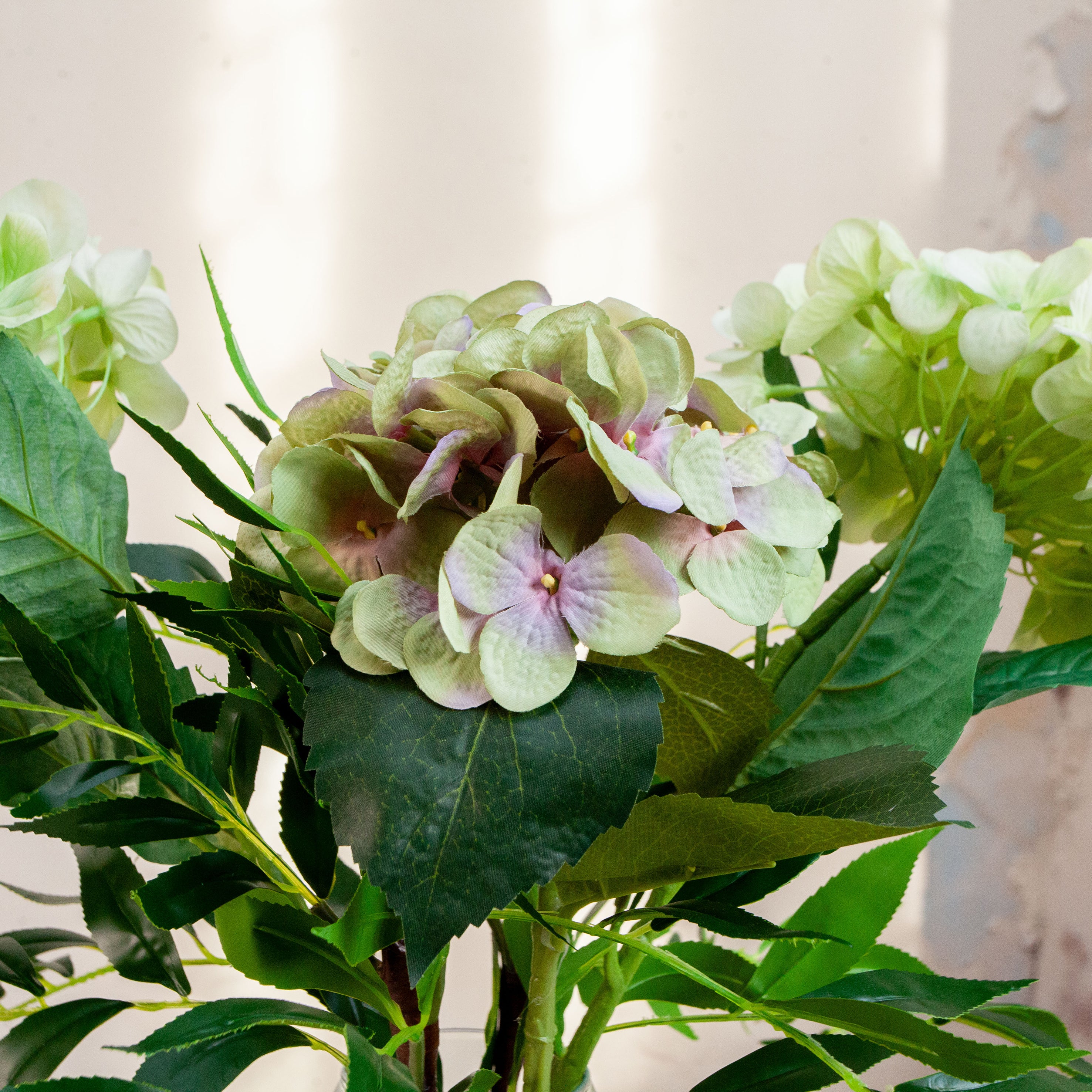 Artificial hydrangea and greenery arrangement in a teardrop-shaped vase,