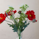 Close-up of artificial red poppies and patrinia with realistic green foliage.
