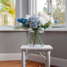 Artificial hydrangea and rose arrangement with soft greenery displayed in a large clear glass Chelsea vase,