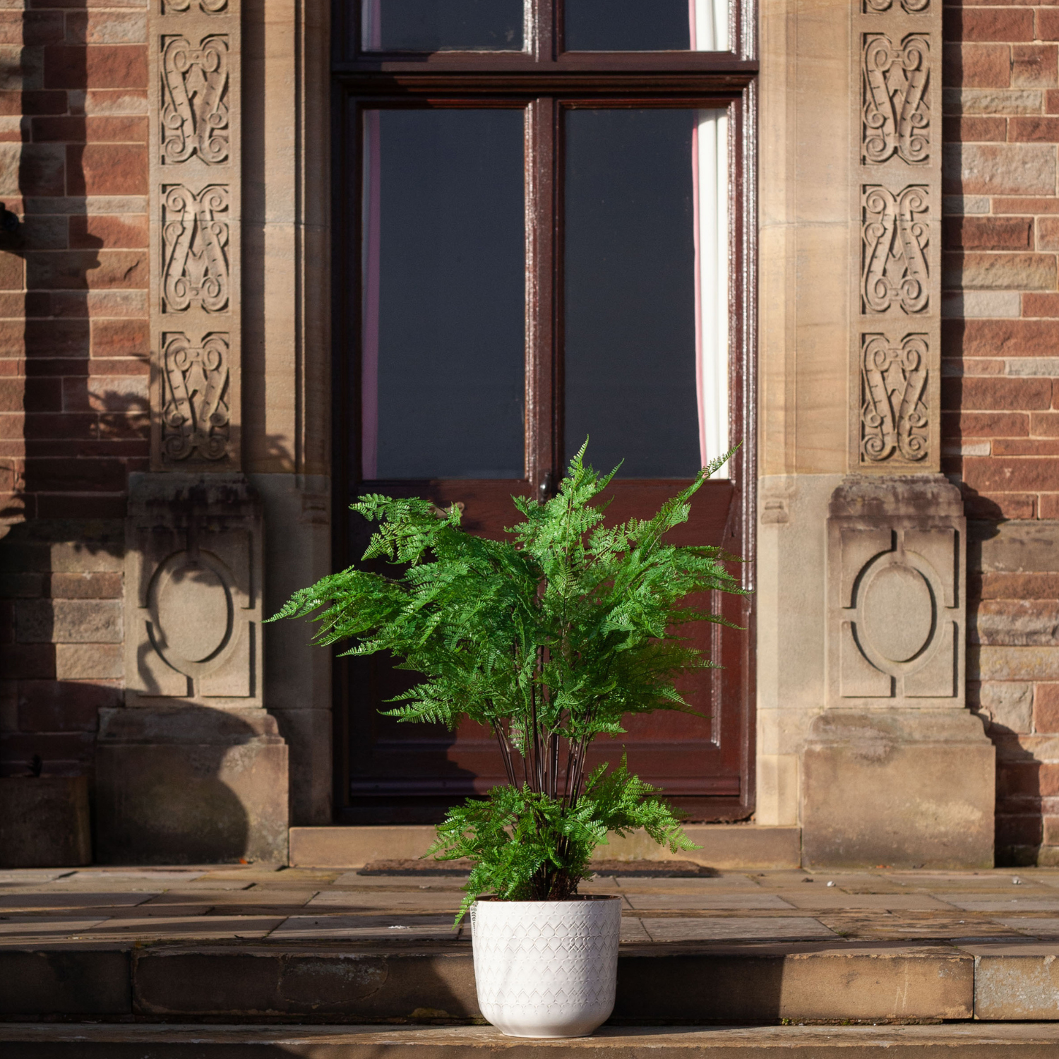 Artificial fern arrangement with lush green fronds displayed in a decorative engraved pot